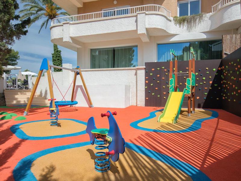 Barevné dětské hřiště se skluzavkou a houpačkami před hotelem.
