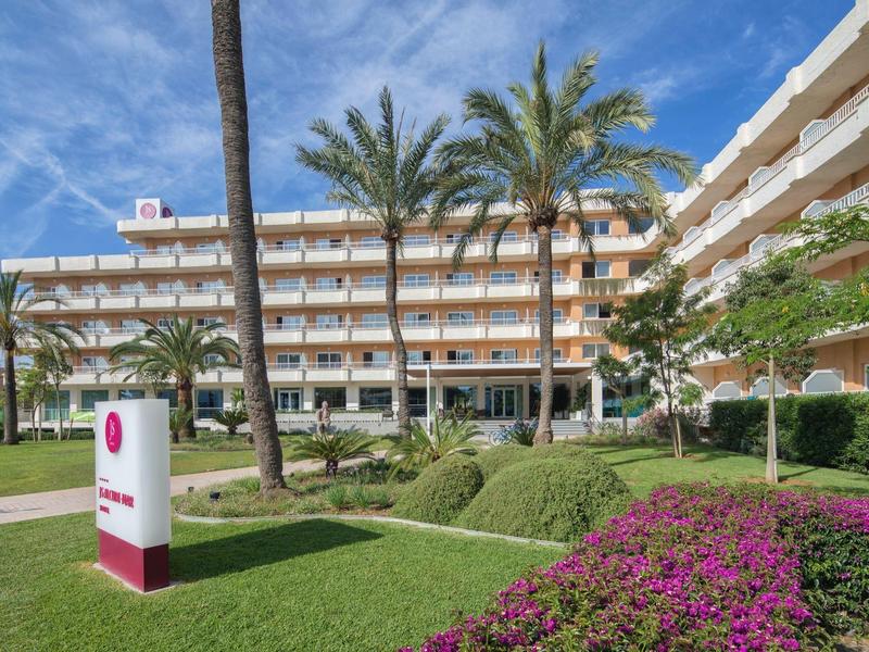 Moderní hotelový komplex s palmami, upraveným trávníkem a květinami pod modrou oblohou