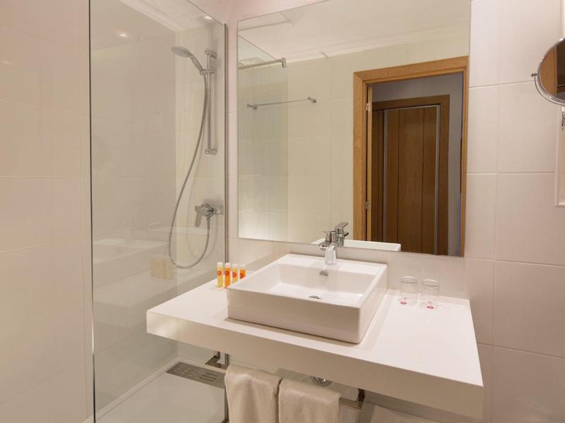 Moderní koupelna s bílým umyvadlem, velkým zrcadlem a sprchovým koutem se skleněnou stěnou.