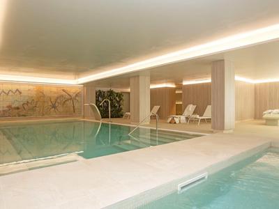 Binnenzwembad met ligstoelen en warme verlichting in een hotel spa-omgeving.