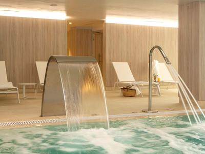 Overdekt zwembad met watervallen en witte ligstoelen tegen houtpanelen.