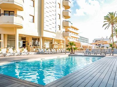 Moderner Hotelpool mit Liegestühlen und Palmen neben einem mehrstöckigen Gebäude.