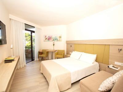 Lichte hotelkamer met tweepersoonsbed, bureau, stoelen, tv en balkon met glazen deur.