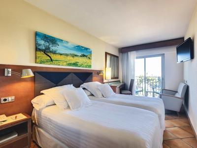 Světlý hotelový pokoj se dvěma postelemi, balkonem, moderním zařízením a výhledem ven.