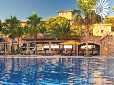 Gran piscina frente a un hotel con palmeras y un molino de viento al fondo.