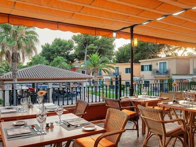 Restauranční terasa s výhledem na bazén obklopený palmami pod oranžovou pergolou.