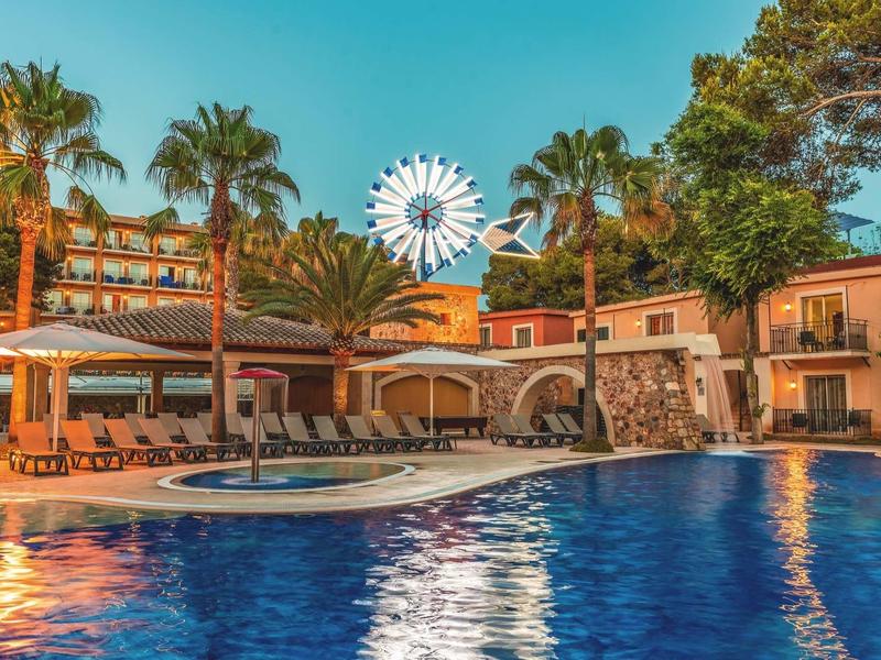 Bazén před hotelem s deštníky, palmami a ruským kolem v pozadí.