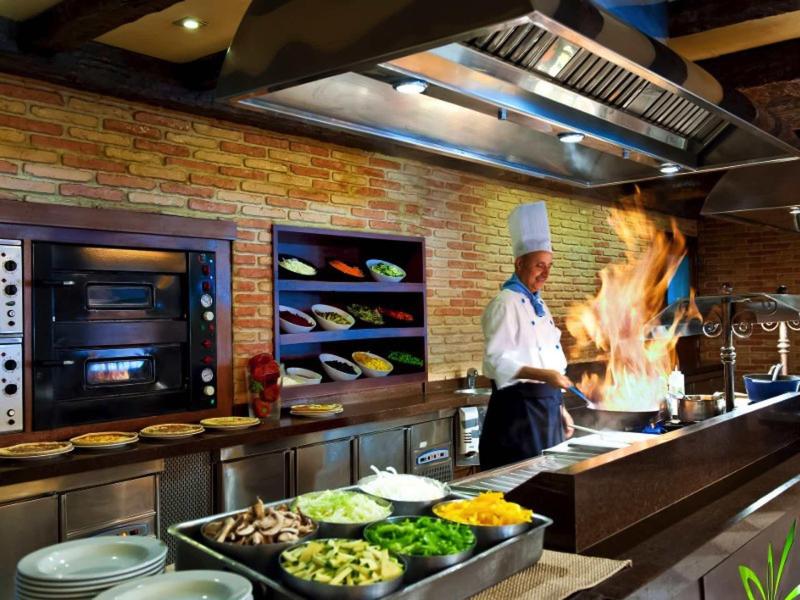 Šéfkuchař v profesionální kuchyni s aktivním plamenem vaření.