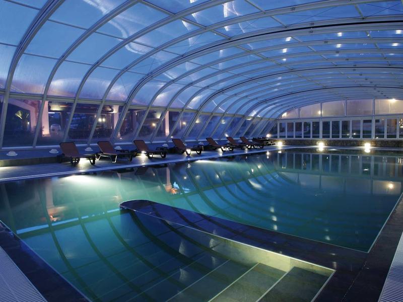 Vnitřní bazén pod moderní prosklenou kopulí osvětlený v noci.