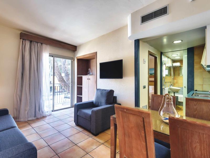 Světý obývací pokoj s pohovkou, křeslem, jídelním stolem, balkonem a vybavenou kuchyní.