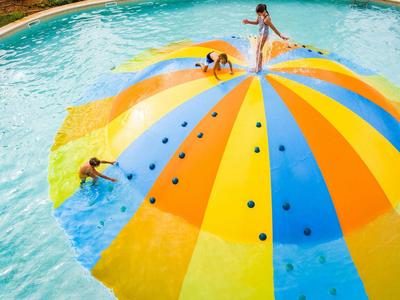 Drei Kinder spielen auf einer bunten, halbkugelförmigen Wasserplattform im Pool.