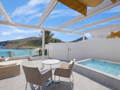 Helle Terrasse mit Whirlwanne, Sitzbereich und Blick auf das Meer und die Berge.