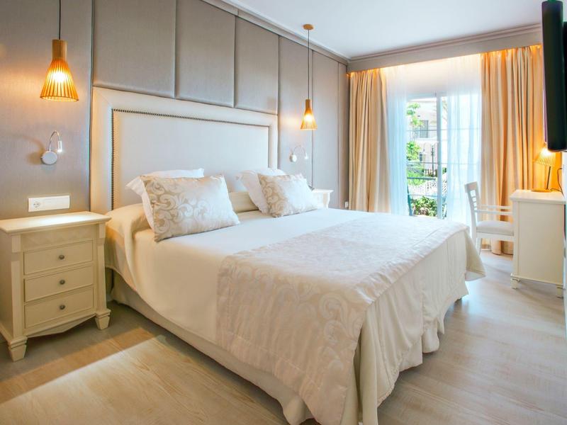 Camera d'hotel luminosa con letto matrimoniale, comodino, sedia e grandi finestre con tende.