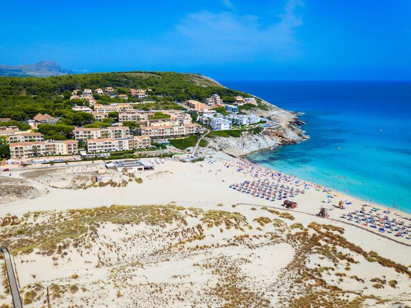 Spiaggia con ombrelloni, vista sull'hotel e mare turchese sotto un cielo azzurro limpido.