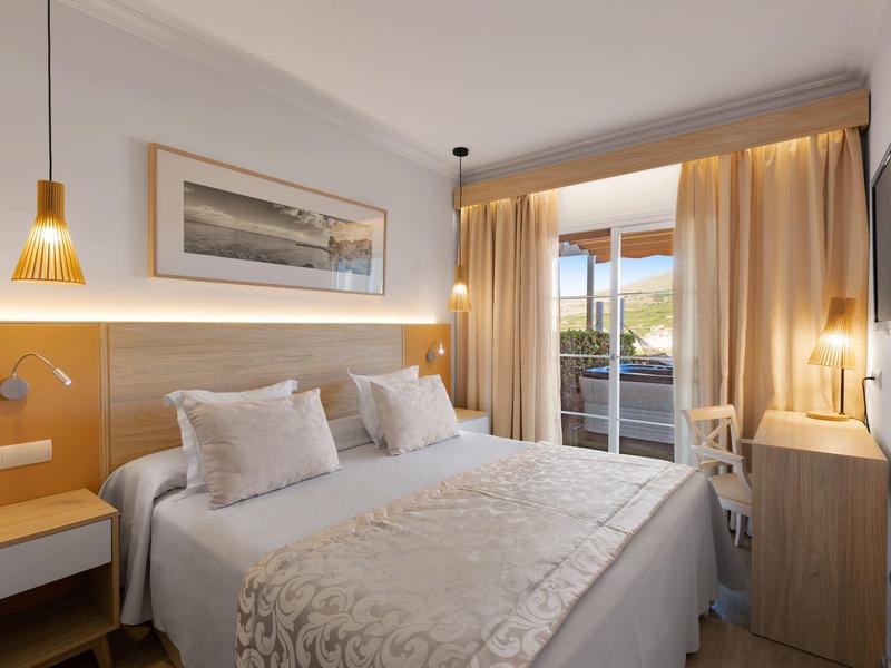 Camera d'hotel moderna con letto matrimoniale, zona salotto e balcone con vista sul paesaggio.