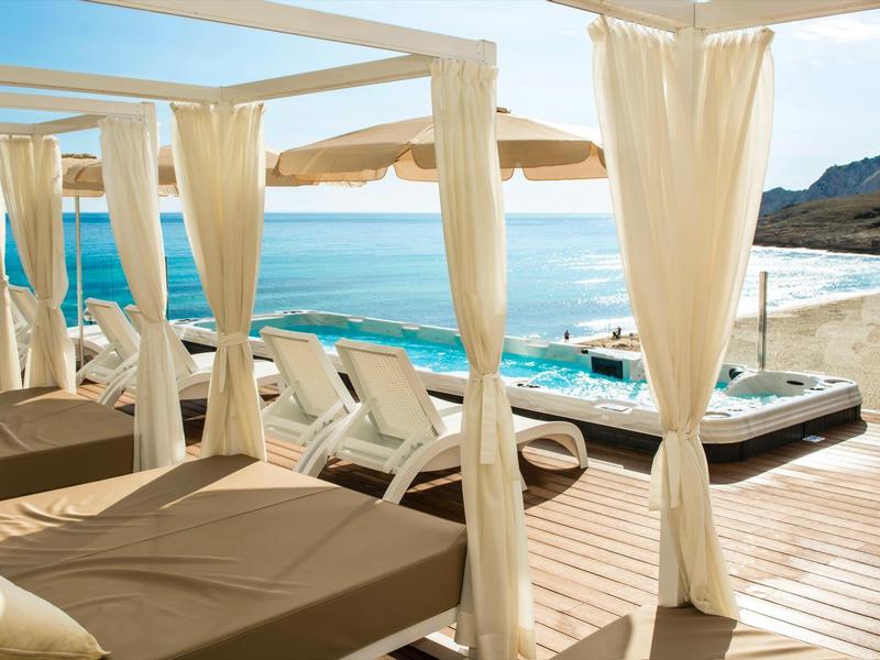 Lounge sulla spiaggia con tende bianche, lettini e vista sul mare blu.