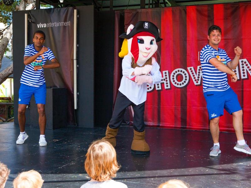 Due ballerini in abiti a righe blu ballano accanto a una grande mascotte su un palco.
