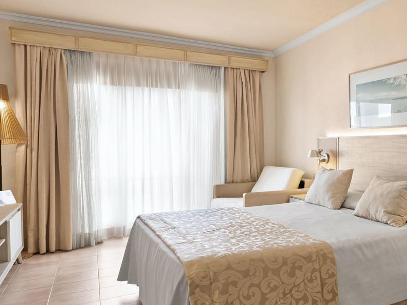 Camera d'hotel luminosa con letto matrimoniale, tende e illuminazione accogliente.