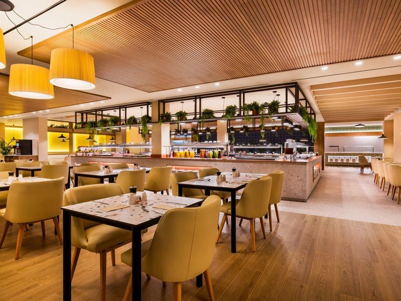 Ristorante luminoso e moderno con pavimenti in legno e sedie gialle in un hotel.