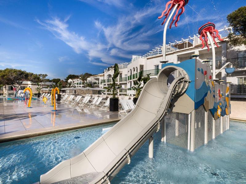 Scivolo d'acqua per bambini con accesso diretto alla piscina in un moderno resort alberghiero sotto cieli sereni.