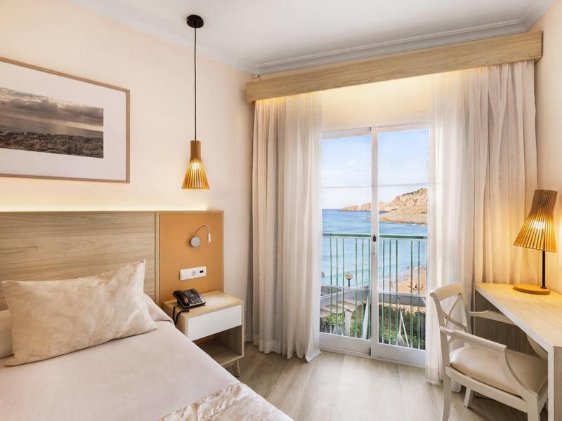 Camera d'hotel luminosa con letto, scrivania e vista mare dalla finestra.