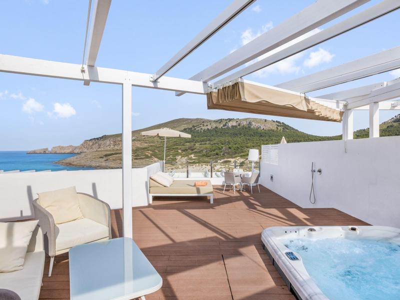 Terrazza con vasca idromassaggio, zona salotto e vista su spiaggia e lago con cielo sereno.