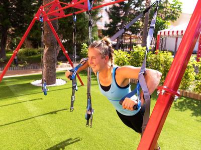 Donna si allena con anelli all'aperto su un parco giochi con erba artificiale verde.