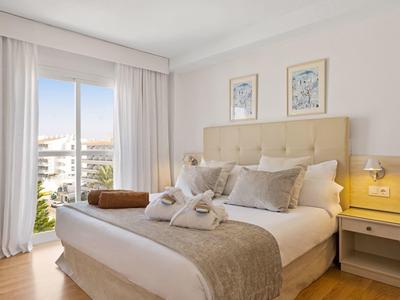 Helles, modernes Schlafzimmer mit großem Bett, weichen Kissen und Blick auf ein Stadtpanorama.