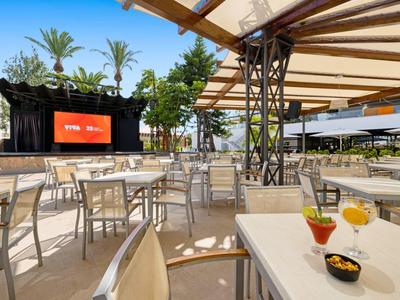 Moderner Außenbereich mit Tischen, Stühlen, einem großen Bildschirm und Getränken auf dem Tisch.