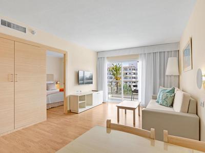 Helles Wohnzimmer mit Sofa, Holzmöbeln und Zugang zum Balkon mit Blick auf umliegende Gebäude.