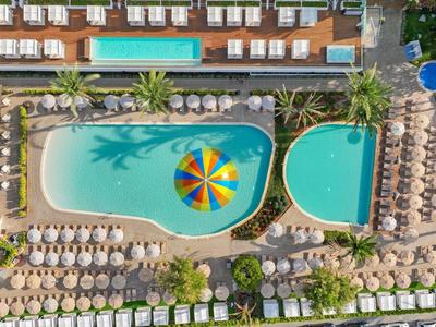 Luftaufnahme eines Hotelpools mit vielen Sonnenschirmen und Liegen in einer Urlaubsanlage.