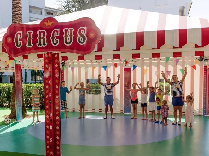 Kinder stehen unter einem rot-weißen Zirkuszelt mit einem Schild 'Circus'.