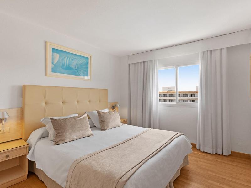 Helles Schlafzimmer mit Doppelbett, beigen Vorhängen, Holzboden und Wandbild an der Wand.