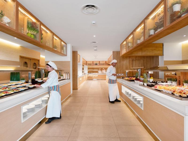 Zwei Köche in einer geräumigen, modernen Buffetküche mit hellem Holz und verschiedenen Speisen.