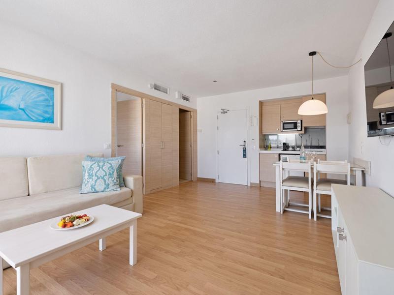 Helles Wohnzimmer mit weißem Sofa, Kaffeetisch, Esstisch und offener Küche mit moderner Ausstattung.