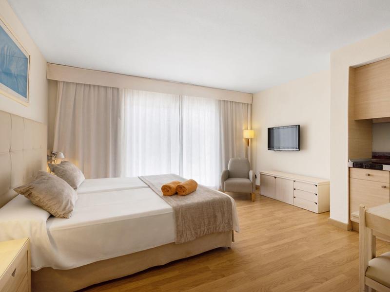 Modernes Hotelzimmer mit Doppelbett, hellem Holzfußboden und einem kleinen Essbereich.