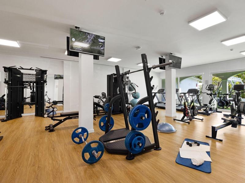 Moderner Fitnessraum mit Kraft- und Cardiogeräten und Holzboden in einem Hotel.