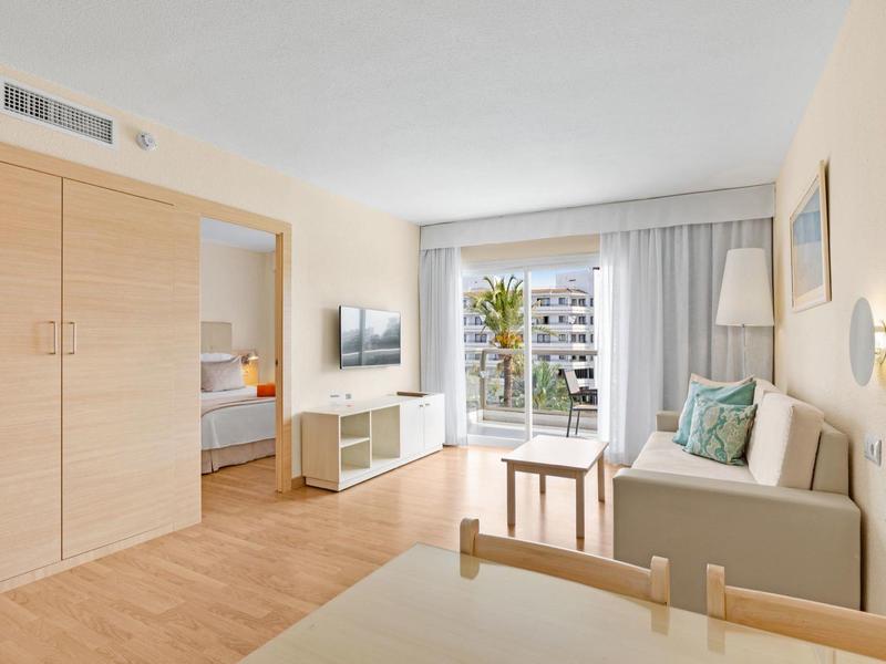 Helles Wohnzimmer mit Sofa, Holzmöbeln und Zugang zum Balkon mit Blick auf umliegende Gebäude.