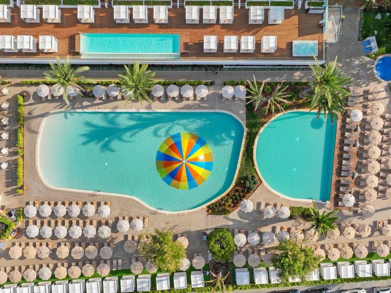 Luftaufnahme eines Hotelpools mit vielen Sonnenschirmen und Liegen in einer Urlaubsanlage.