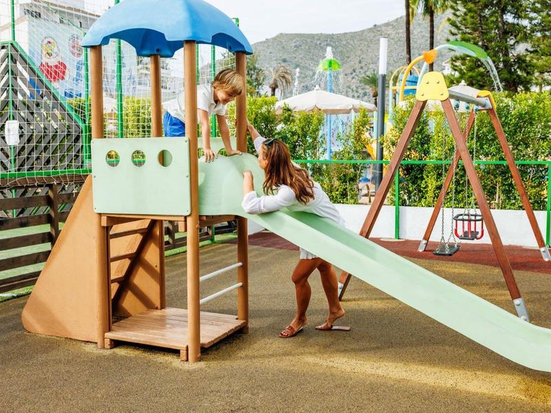 Kind spielt auf einem Spielplatz mit Rutsche und Schwunggerüst im Freien.