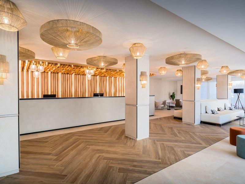 Moderní hotelová recepce s bílým pultem, dřevěnou podlahou a elegantním osvětlením.