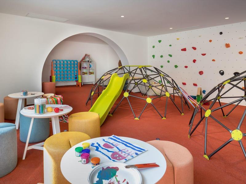 Barevná dětská herna s klouzačkou, stoly a horolezeckou stěnou v hotelu.