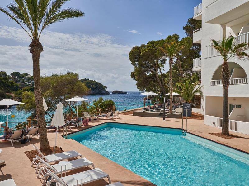 Venkovní bazén s lehátky a výhledem na moře, bílé slunečníky.