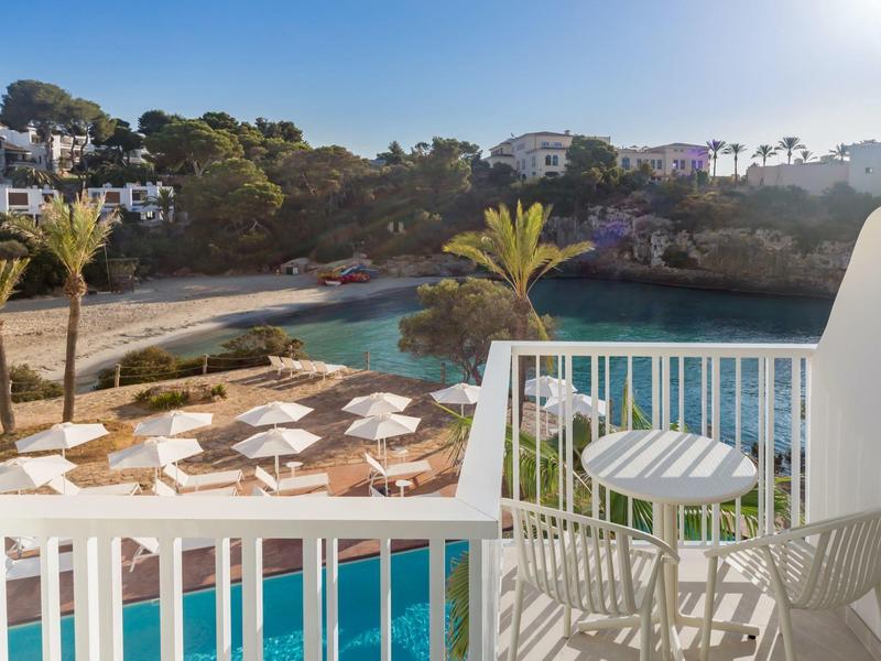 Balkon s stolem a židlemi s výhledem na bazén a pláž se slunečníky.