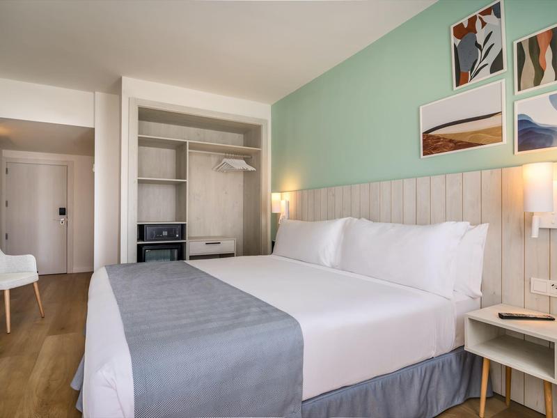 Moderní hotelový pokoj s dvoulůžkem, zelenými stěnami a bílou židlí.