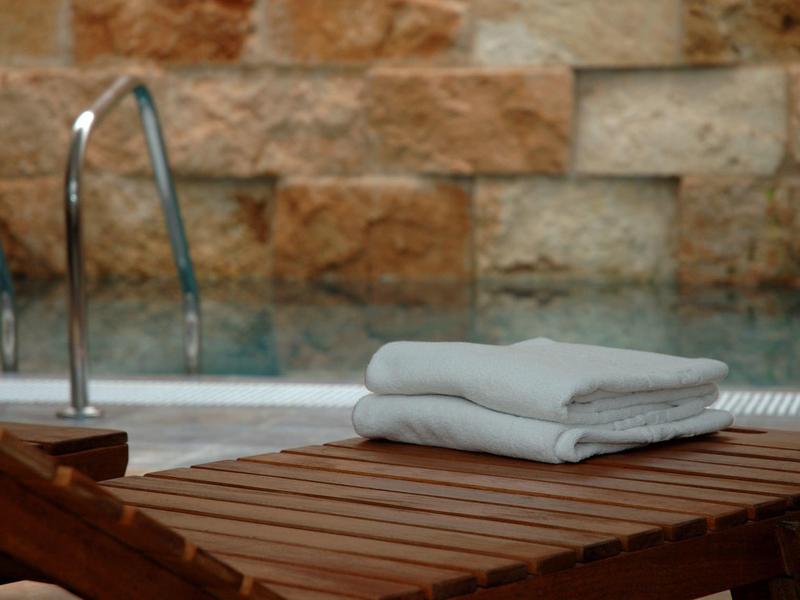 Složení bílé ručníky na dřevěném lehátku u bazénu s kamennou zdí.