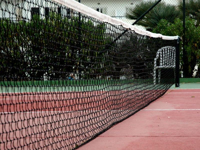 Tenisový kurt s koulí, hotel v pozadí pod jasnou oblohou.