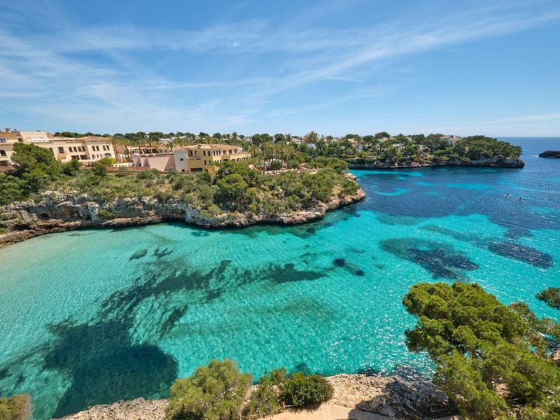 Malebná zátoka s průzračně tyrkysovou vodou a bujnou vegetací na skalnatém pobřeží.