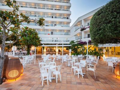 Espace extérieur d'un hôtel avec des chaises blanches et des tables sur une terrasse au crépuscule.