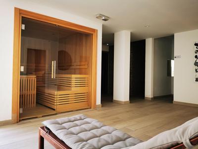 Espace sauna moderne avec porte vitrée et chaise longue confortable dans une pièce lumineuse.